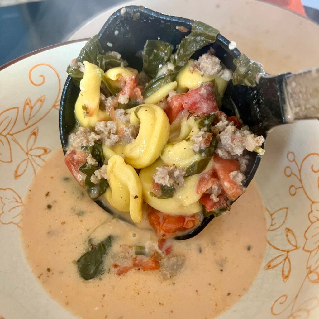 A ladle of tortellini soup with spinach and tomatoes